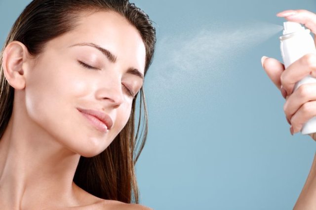Beautiful woman applying spray  water treatment on face